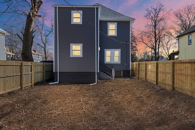 back of house at dusk with entry steps, a shingled roof, and a fenced backyard