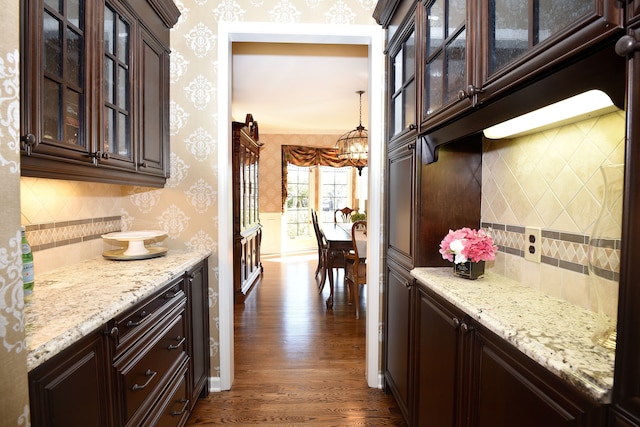 kitchen featuring dark wood-style flooring, dark brown cabinets, a chandelier, wallpapered walls, and tasteful backsplash
