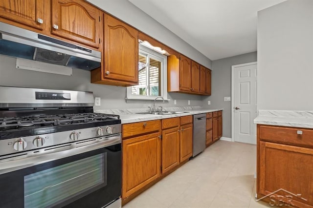 kitchen featuring brown cabinetry, a sink, light countertops, under cabinet range hood, and stainless steel appliances