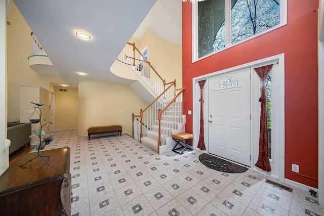 entrance foyer with visible vents, baseboards, stairs, and a high ceiling