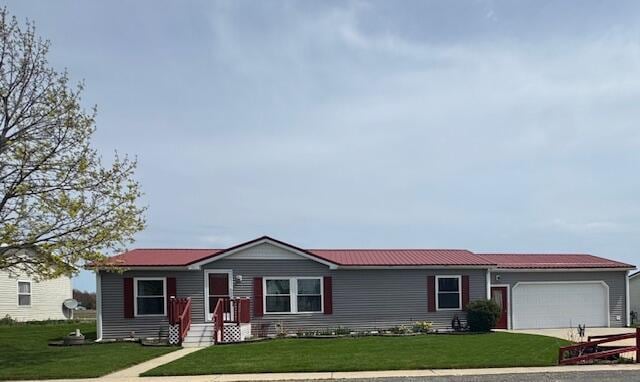ranch-style house with an attached garage, concrete driveway, metal roof, and a front yard