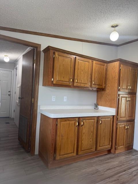 kitchen with light countertops, ornamental molding, brown cabinetry, and a textured ceiling