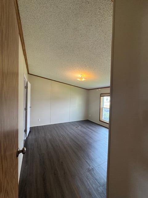 empty room with crown molding, dark wood finished floors, and a textured ceiling