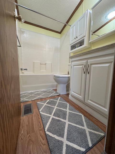 bathroom featuring a textured ceiling, visible vents, crown molding, wood finished floors, and toilet