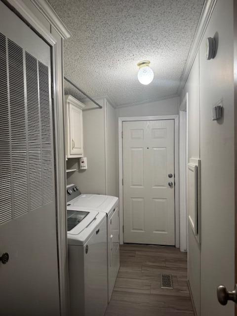 washroom featuring cabinet space, a textured ceiling, a heating unit, visible vents, and washing machine and dryer