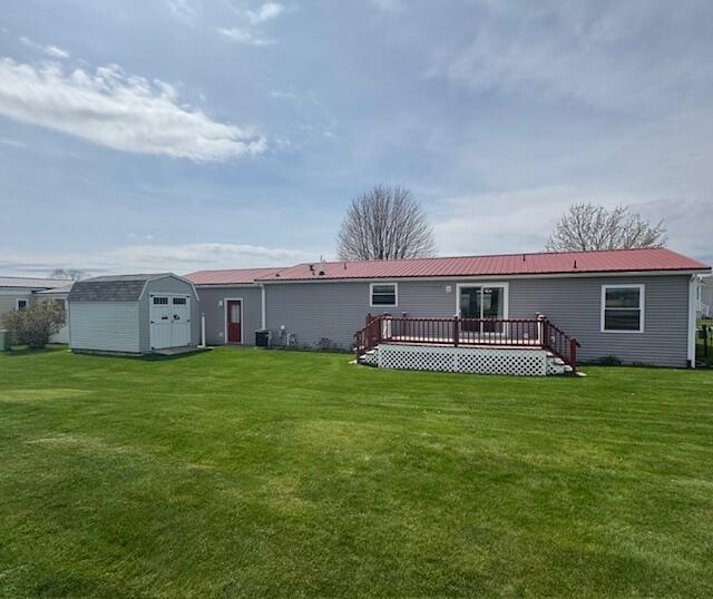 rear view of house featuring a storage shed, a wooden deck, an outbuilding, a yard, and metal roof
