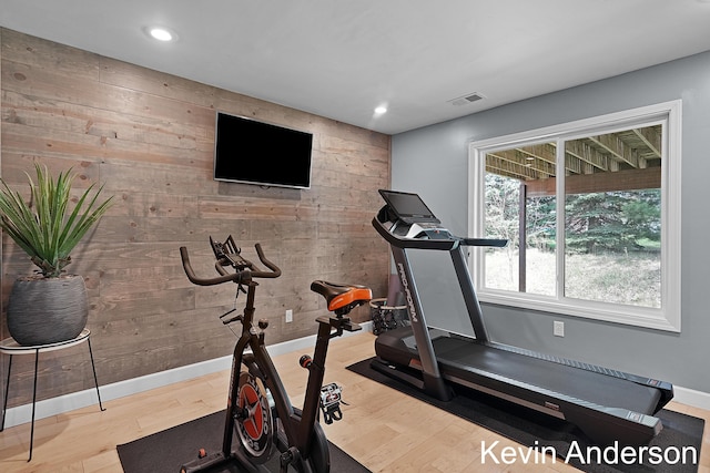 workout room with baseboards, wood walls, and wood finished floors