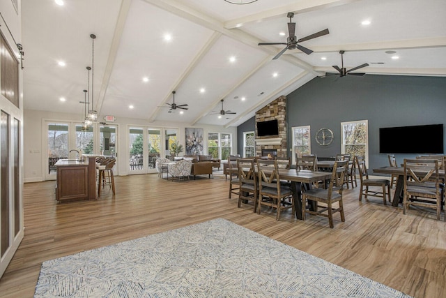 dining area with light wood-type flooring, a ceiling fan, a fireplace, and beamed ceiling