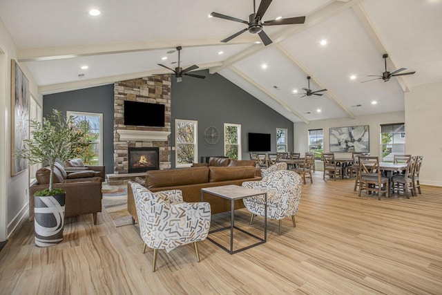 living area featuring a fireplace, ceiling fan, beamed ceiling, and light wood-style flooring
