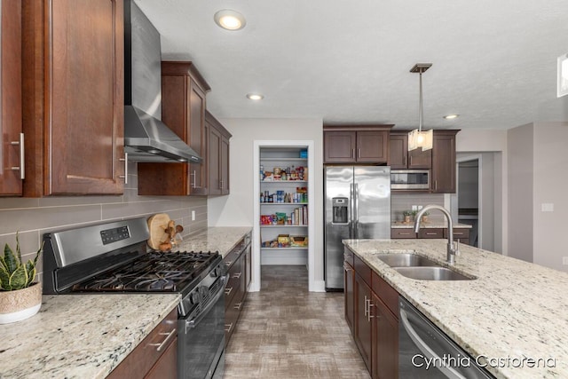 kitchen with decorative backsplash, appliances with stainless steel finishes, a sink, light stone counters, and wall chimney exhaust hood
