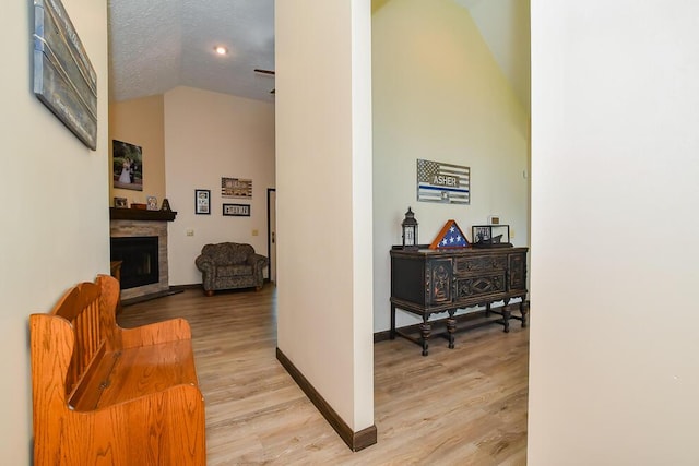 hallway featuring baseboards, light wood-style flooring, and high vaulted ceiling