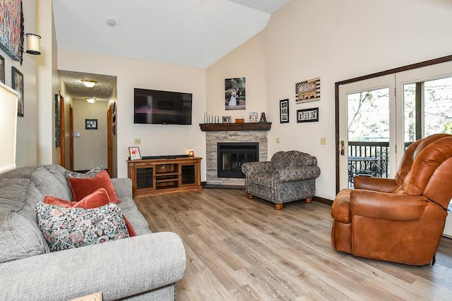 living room with high vaulted ceiling, a stone fireplace, baseboards, and light wood-type flooring
