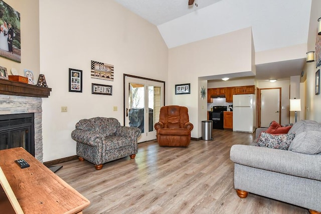 living room with light wood-style floors, baseboards, a stone fireplace, ceiling fan, and high vaulted ceiling