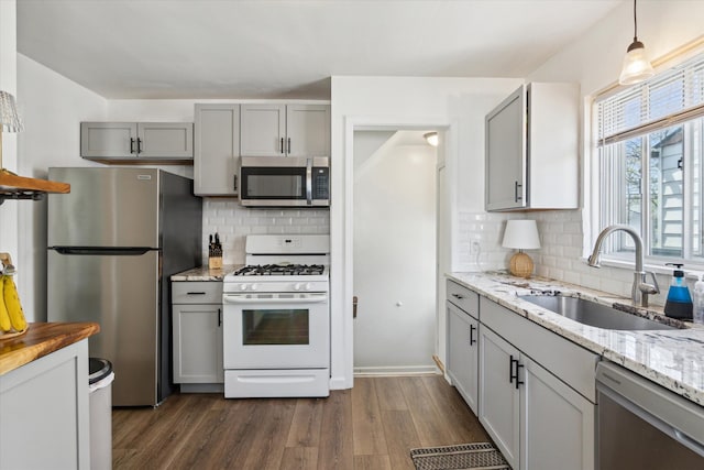 kitchen with dark wood-style flooring, tasteful backsplash, a sink, gray cabinetry, and stainless steel appliances