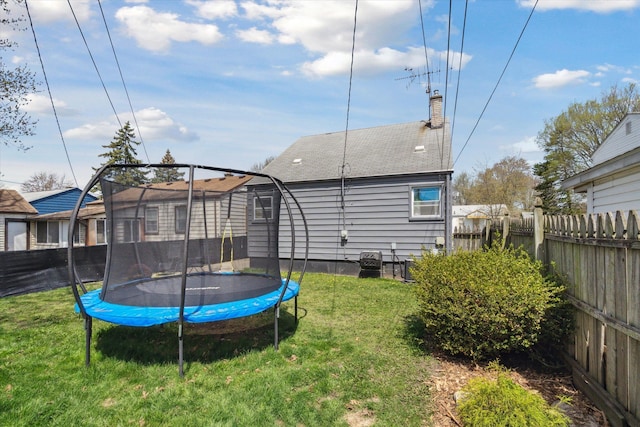 back of house featuring a lawn, a trampoline, fence, and a chimney