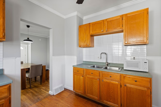 kitchen featuring visible vents, white microwave, tasteful backsplash, a sink, and dark wood finished floors