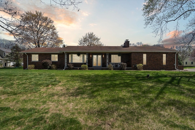 back of house with a yard, brick siding, and a chimney