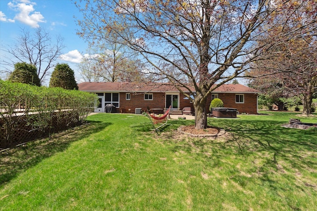 back of property featuring brick siding, a hot tub, and a yard