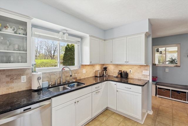 kitchen with a sink, dark stone counters, backsplash, stainless steel dishwasher, and glass insert cabinets