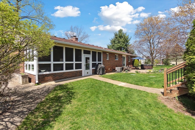 back of house featuring a patio, a chimney, brick siding, central air condition unit, and a yard