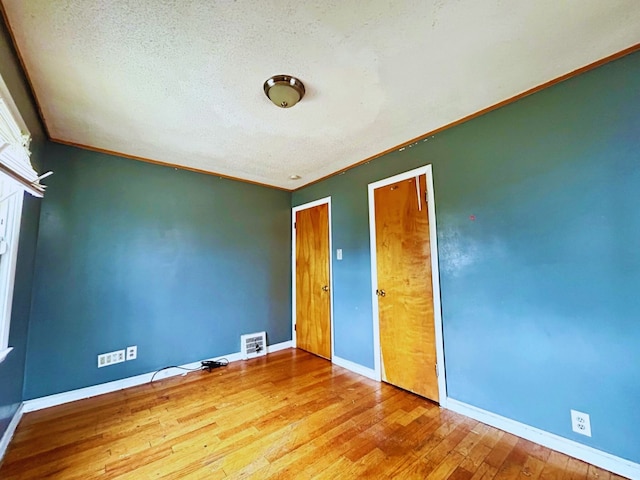 unfurnished bedroom featuring crown molding, a textured ceiling, visible vents, baseboards, and hardwood / wood-style flooring