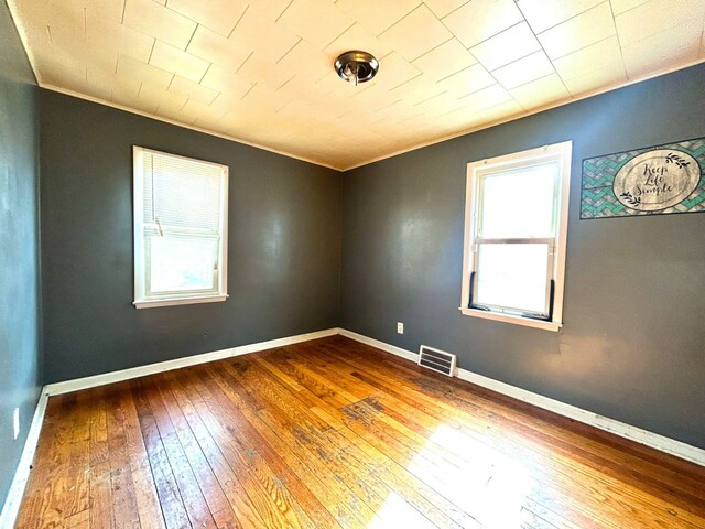 spare room featuring ornamental molding, hardwood / wood-style flooring, baseboards, and visible vents