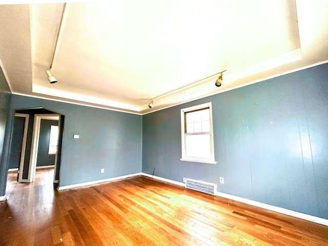 unfurnished room with hardwood / wood-style floors, rail lighting, visible vents, a tray ceiling, and baseboards