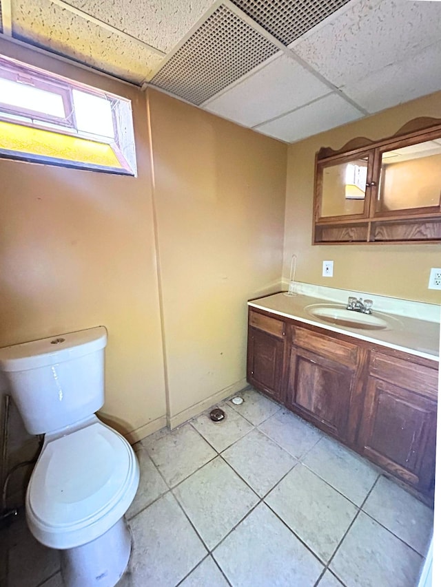 half bathroom featuring a paneled ceiling, vanity, toilet, and tile patterned flooring