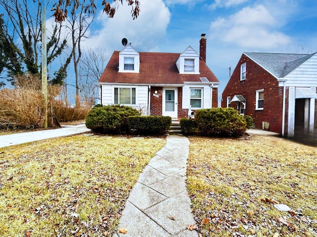 cape cod-style house featuring a chimney, a front yard, and brick siding