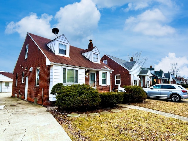 new england style home featuring a chimney and brick siding