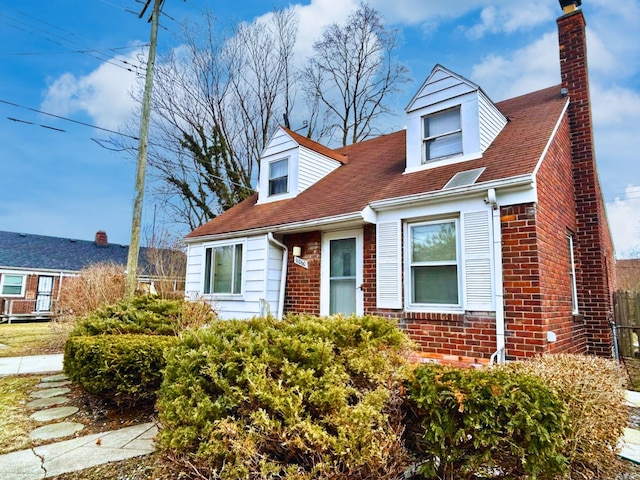 cape cod home with brick siding, a chimney, and fence