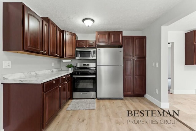 kitchen featuring a textured ceiling, light countertops, baseboards, light wood finished floors, and stainless steel appliances