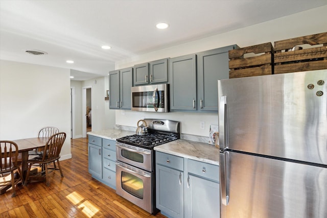 kitchen with visible vents, hardwood / wood-style flooring, light stone counters, stainless steel appliances, and recessed lighting