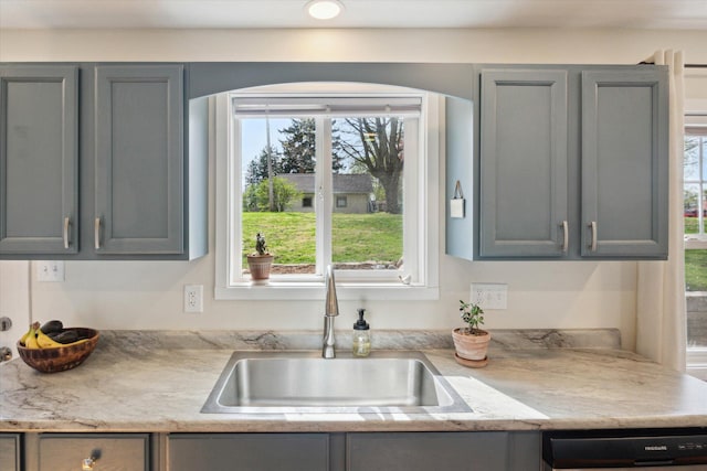 kitchen with gray cabinetry, light countertops, dishwashing machine, and a sink