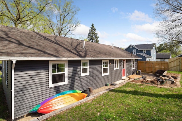 back of house featuring fence, a lawn, and roof with shingles