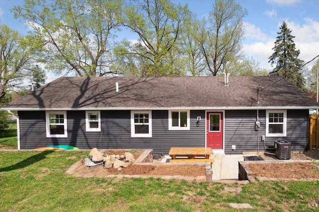 rear view of property featuring a lawn, central AC unit, fence, and a shingled roof