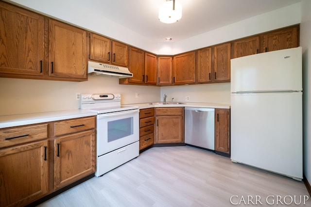 kitchen with brown cabinetry, a sink, under cabinet range hood, and white appliances