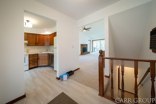 kitchen featuring brown cabinets, a sink, a fireplace, white appliances, and a ceiling fan