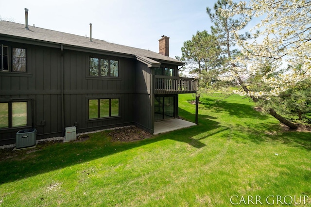 rear view of property with board and batten siding, a chimney, a wooden deck, central air condition unit, and a yard