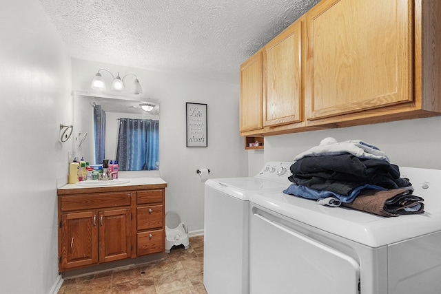 laundry room with a textured ceiling, cabinet space, a sink, baseboards, and washer and clothes dryer