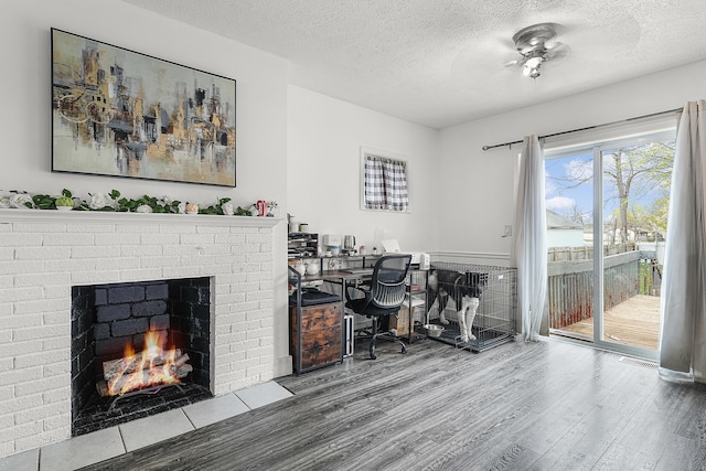 home office with visible vents, a brick fireplace, wood finished floors, ceiling fan, and a textured ceiling