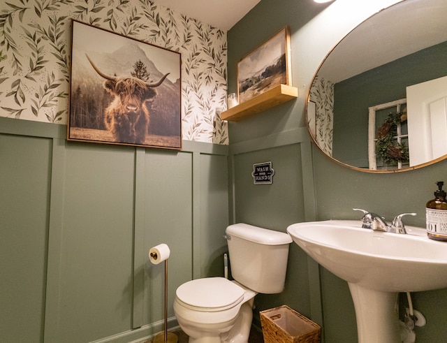 bathroom featuring a decorative wall, a wainscoted wall, toilet, and wallpapered walls