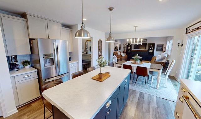 kitchen featuring stainless steel fridge, light countertops, light wood-style flooring, decorative light fixtures, and a kitchen island