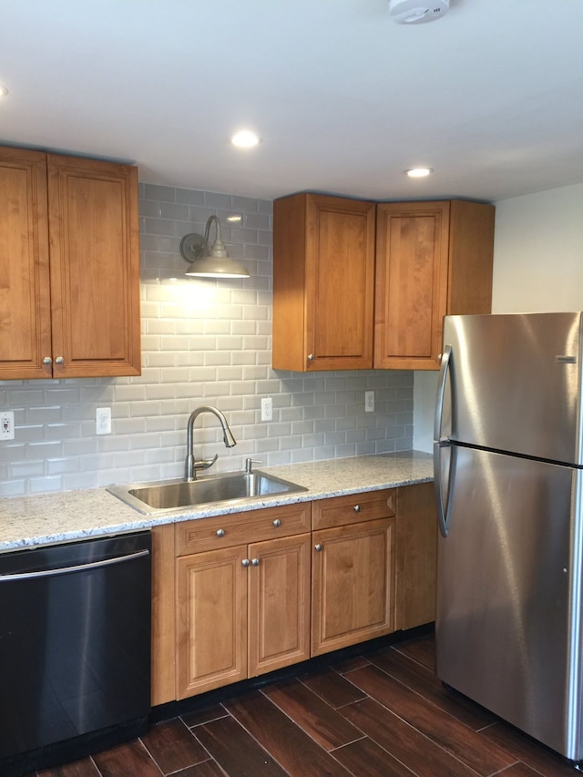 kitchen featuring brown cabinets, a sink, dark wood finished floors, freestanding refrigerator, and dishwashing machine