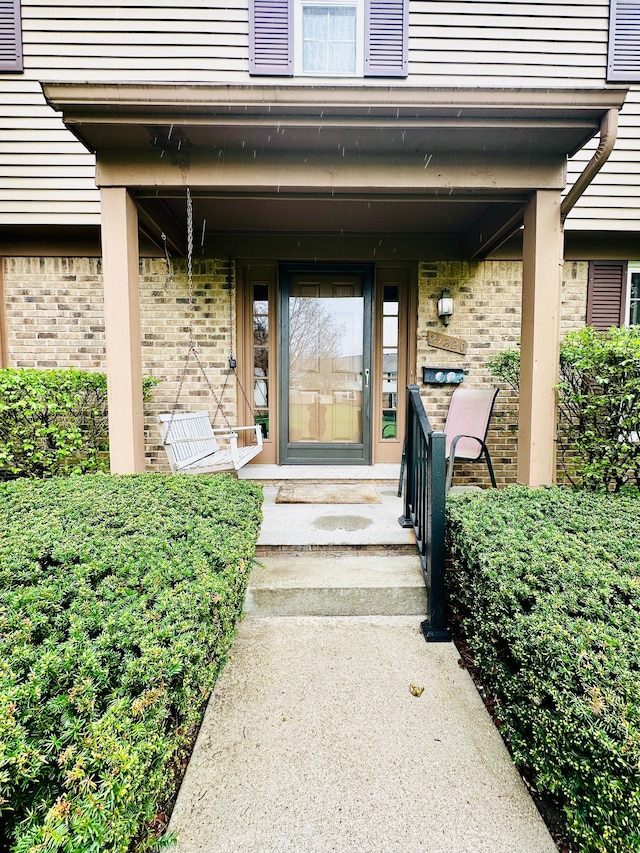 doorway to property featuring covered porch and brick siding