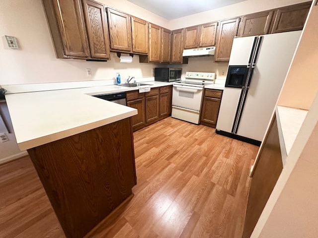 kitchen with a peninsula, white appliances, light countertops, under cabinet range hood, and light wood finished floors