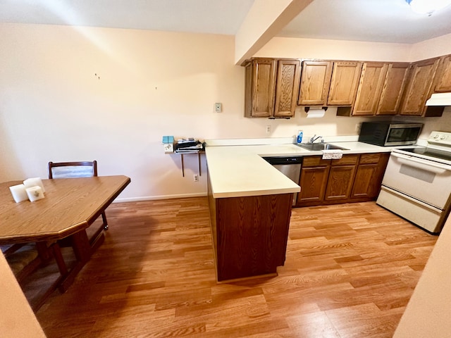kitchen featuring brown cabinetry, a peninsula, light wood-type flooring, light countertops, and stainless steel appliances