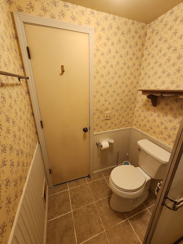 bathroom with tile patterned flooring, wainscoting, toilet, and wallpapered walls
