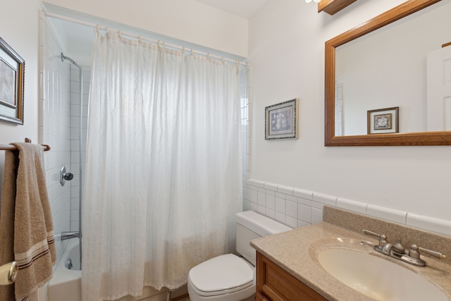 bathroom with vanity, wainscoting, toilet, tile walls, and shower / bath combo