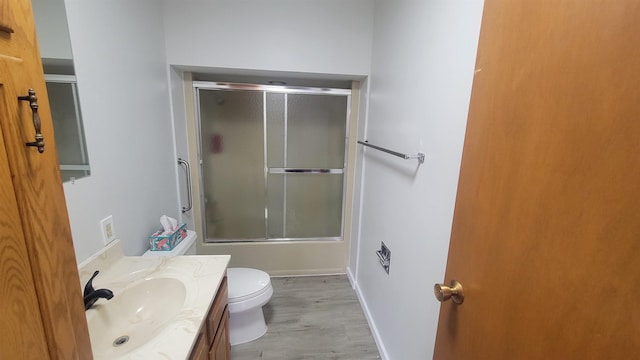 bathroom featuring vanity, wood finished floors, toilet, baseboards, and enclosed tub / shower combo